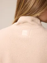 Canguro de sherpa color bordó, con cuello alto y cierre frontal parcial. Presenta un bolsillo con cierre en el pecho y bolsillos laterales, confeccionado en tejido de textura suave y abrigada.