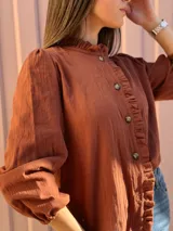 Camisa de manga larga color marrón chocolate, con cuello alto y detalles de volados a lo largo de la botonadura frontal.