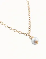 Dije colgante dorado con una perla blanca.
