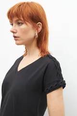 Remera negra de corte recto, con cuello en V y detalle de trenzas en los hombros.