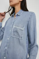 Camisa celeste de denim tencel, de corte holgado, con cuello clásico, cierre frontal con botones y bolsillo en el pecho con detalle bordado.