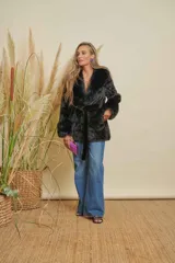 Abrigo negro de piel sintética con cuello solapa, manga larga y cinturón de tela para ajustar en la cintura.