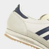 Championes Adidas SL 72 OG de color beige, con las icónicas tres tiras y detalles en azul marino. Cuentan con suela de caucho texturizada y doble cordón en tonos celeste y azul con puntos blancos.