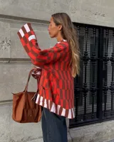 Saco tejido de punto con diseño de cuadros en tonos rojo, marrón y rosa claro. Presenta corte recto oversize, cierre frontal con botones en forma de corazón y dos bolsillos delanteros.