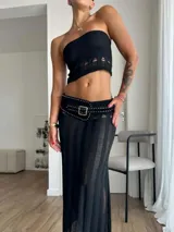 Conjunto de dos piezas compuesto por un top corto tipo strapless con detalle de aberturas en el ruedo y una falda larga de tiro medio con transparencias, aberturas en la cintura y cinturón incorporado con tachas y hebilla metálica.