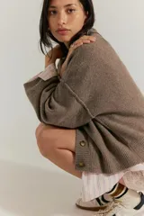 Cárdigan de silueta oversized confeccionado en hilo de algodón, color beige. Presenta escote en V, cierre frontal con botones, hombros caídos y mangas largas amplias con terminaciones acanaladas.