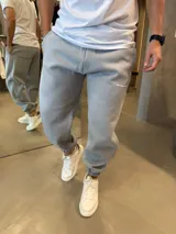 Pantalón de jogging gris claro con puños elásticos en los tobillos, bolsillos laterales y logo de la marca estampado en la pierna. Confeccionado en algodón premium con textura suave.