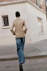 Blazer cruzado color beige, de manga larga, con cuello solapa y forro interior negro. Presenta cierre frontal con botones dorados y bolsillos de vivo en el pecho y bolsillos con solapa en el delantero.