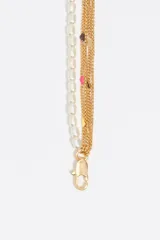 Pulsera de diseño multicadena que combina una hilera de perlas de resina blancas con varias cadenas finas de latón dorado. Presenta un dije circular con logo grabado y pequeños detalles decorativos en esmalte de colores. Cuenta con un cierre de mosquetón metálico.