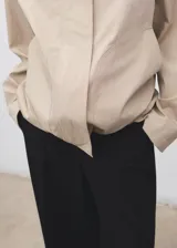 Chaqueta oversize color beige con cuello camisero de pana en contraste color negro. Presenta cierre frontal oculto con cremallera y botones, manga larga y bajo con cordón interior ajustable.