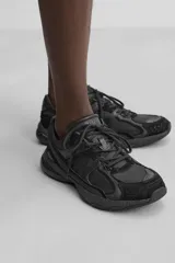 Zapatilla deportiva tipo running de color negro, perteneciente a la colección especial Origins. Presenta una parte superior confeccionada en una combinación de cuero con acabado de gamuza y tejido transpirable. Cuenta con una suela de volumen con diseño irregular y cierre mediante cordones.