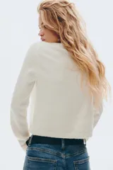 Cárdigan de punto fino, color blanco, de manga larga y corte corto (cropped). Presenta escote redondo y cierre frontal con botones nacarados.