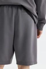 Short de felpa interlock color gris oscuro, con cintura elástica fruncida y cordón ajustable. Presenta un diseño de corte relajado a la rodilla, bolsillos laterales y bolsillos traseros.