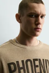 Sudadera de corte relajado confeccionada en tejido con textura waffle, color beige con efecto lavado. Presenta cuello redondo, manga larga con franjas laterales oscuras y estampado frontal con texto y número en contraste.