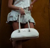 Cartera baguette de cuero marrón con manijas largas y detalle de nudos esféricos de alpaca en la unión de las manijas.