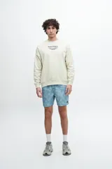 Buzo celeste de corte holgado con cuello redondo y puños y cintura acanalados. Estampado frontal con texto "Sunset Whispers" en color azul.