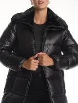 Campera puffer larga de acabado satinado en color beige. Presenta un diseño capitoneado horizontal, cuello amplio revestido en piel sintética, cierre frontal bidireccional y bolsillos laterales con cremallera.