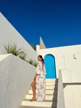 Vestido corto blanco con estampado floral en tonos naranja y verde, escote en V con detalle de nudo, mangas largas acampanadas y falda con volantes y abertura lateral.