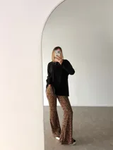 Pantalón tipo oxford de tiro alto con estampado animal print de leopardo, corte ajustado en la parte superior y acampanado desde la rodilla hacia abajo.