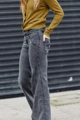 Jean de tiro medio con corte acampanado, confeccionado en denim gris oscuro con efecto lavado. Presenta costuras decorativas y detalles de bordado en la zona de la cintura y bolsillos.