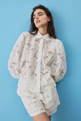 Camisa de broderie color blanco, con cuello clásico, mangas abullonadas y cierre frontal oculto.