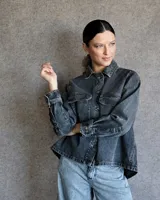 Sobrecamisa de denim gris con cuello camisero, cierre frontal con botones, mangas largas con puños abotonados, dos bolsillos con solapa en el pecho y corte holgado.
