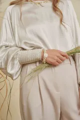 Blusa de satén color champagne con cuello a la base, mangas anchas y puños elásticos con detalle bordado.