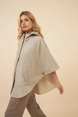 Capa amplia con capucha, confeccionada en lana fina sin teñir. Presenta cierre frontal, bolsillos delanteros y botones laterales que permiten ajustar la forma de las mangas.