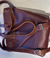 Mochila de cuero marrón con diseño minimalista, silueta estructurada, asas superiores y correas ajustables para la espalda.