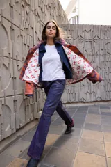 Campera de corte oversize con estampado abstracto en tonos naranja y violeta. Presenta cuello alto tejido en color azul oscuro, cierre frontal con botones metálicos a presión y bolsillos frontales con solapa, uno de ellos con el detalle de la palabra 'CAPER' aplicada.