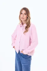 Camisa blanca de manga larga con cuello clásico y cierre frontal de botones negros en contraste. Presenta un bolsillo frontal en el pecho y un diseño de líneas simples y corte recto.