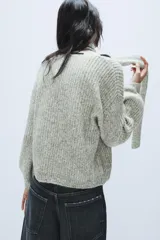 Jersey de punto de corte holgado en color gris jaspeado, con escote en pico y bufanda integrada del mismo tejido. Presenta mangas largas con puños ajustados.