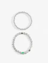 Set de dos pulseras elásticas plateadas. Una de cuentas redondas pequeñas y otra de cuentas planas con un dije de ojo turco verde.