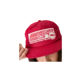 Gorro tipo gorra roja con un parche bordado blanco en la parte frontal que incluye texto y el logotipo de la marca.