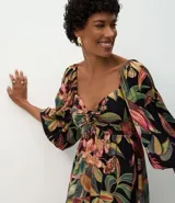 Vestido midi de corte evasé con estampado de follaje tropical sobre fondo negro. Presenta escote corazón, mangas abullonadas y un diseño fluido confeccionado en viscosa.