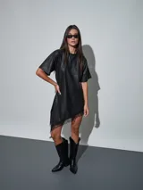 Vestido corto de efecto cuero color negro, de corte recto y holgado, con mangas corta y detalle de encaje negro en el dobladillo asimétrico.