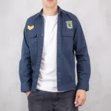 Sobrecamisa azul marino de gabardina con dos bolsillos frontales con botón, charreteras con galones dorados en el hombro izquierdo y parche bordado de las fuerzas especiales en el bolsillo derecho.