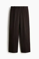 Pantalón sastrero de sarga en color marrón oscuro, con corte holgado, piernas amplias con raya marcada, cierre frontal con botón y corchete ocultos, bolsillos laterales al bies y bolsillos traseros insertados.