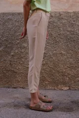 Pantalón chino color beige de lino y viscosa, con bordado de palmeras en verde claro. Tiene tiro medio-alto, pierna recta y bolsillos laterales y traseros.