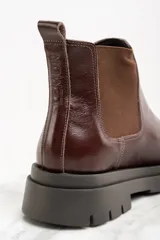 Bota Chelsea de cuero color marrón oscuro con elásticos laterales y suela track negra.