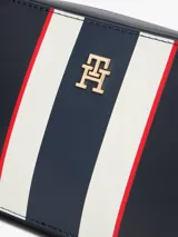 Cartera tipo bandolera de Tommy Hilfiger, confeccionada en poliuretano color azul marino. Presenta un diseño rectangular con una franja vertical central en colores blanco, azul y rojo, y el logo monograma TH en metal dorado en el frente. Incluye correa ajustable y cierre superior.