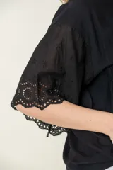 Blusa negra de viscosa con mangas cortas y detalle de broderie en los puños. Tiene cuello redondo y cierre frontal con botones.