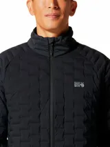 Campera técnica de Mountain Hardwear con aislamiento de plumón, diseñada con tejido elástico para mayor libertad de movimiento. Presenta cierre frontal completo, cuello alto, bolsillos laterales con cierre y diseño acolchado con patrón geométrico.