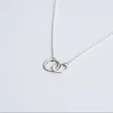 Collar de cadena fina con dije compuesto por dos argollas entrelazadas de plata 925 con acabado pulido.