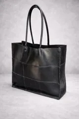 Bolso tote grande de cuero natural en color marrón, con diseño de piezas unidas mediante costuras visibles y asas de hombro.