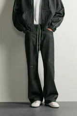 Jeans wide fit de denim negro, con costuras y detalles en color verde claro, bolsillos laterales y traseros, y cintura ajustable con cordón integrado.