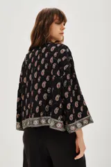 Kimono corto de estilo bohemio, confeccionado en viscosa negra con estampado paisley y detalles bordados en los bordes frontales y mangas. Presenta mangas tres cuartos y un lazo ajustable en la cintura con estampado animal print.
