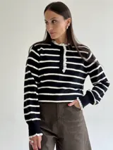 Sweater de punto a rayas horizontales negras y blancas, con cuello redondo y cierre frontal parcial de botones. Presenta detalles de puntilla blanca en el cuello, la tapeta de botones y los puños.
