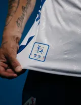 Camiseta de fútbol Umbro del Club Nacional de Football, modelo Home 2025, para hombre. Diseño blanco con detalles en azul y rojo en cuello y mangas. Incluye logo de Umbro, escudo del club y sponsor Antel en el frente.