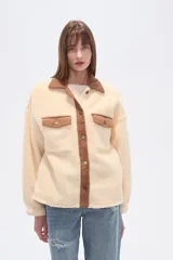 Campera tipo shacket de corderito color crema, con detalles en pana marrón en cuello, solapa de botones y bolsillos frontales. Diseño holgado de manga larga con cierre frontal de botones.